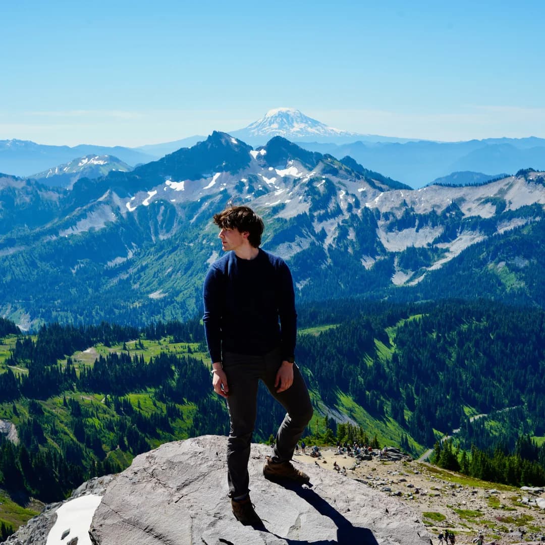 Grant standing on a rocky overlook with Mount Rainier in the distance.